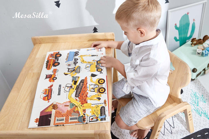 a little boy sitting at a table with a construction themed book